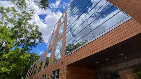 Modern building made of terracotta tiles and large windows reflecting trees and clouds.