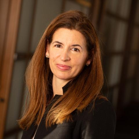 Woman smiling with long brown hair in black blazer and white shirt.