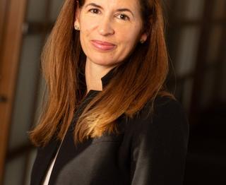 Woman smiling with long brown hair in black blazer and white shirt.