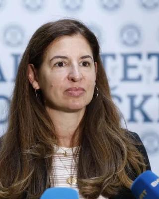 Woman with long brown hair speaking into a microphone.