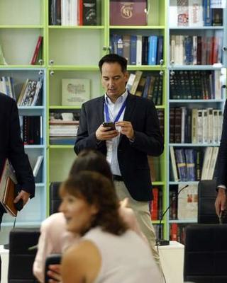Three men in black jackets stand in front of a bookcase.