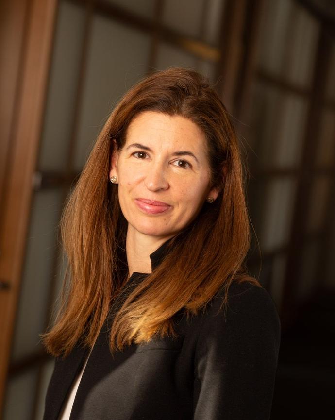 Woman smiling with long brown hair in black blazer and white shirt.